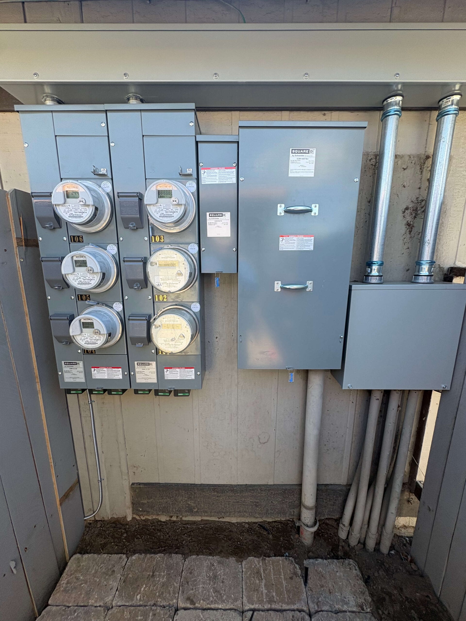 Square D multi-meter pack and main service disconnect panel installed on an exterior utility alcove wall.