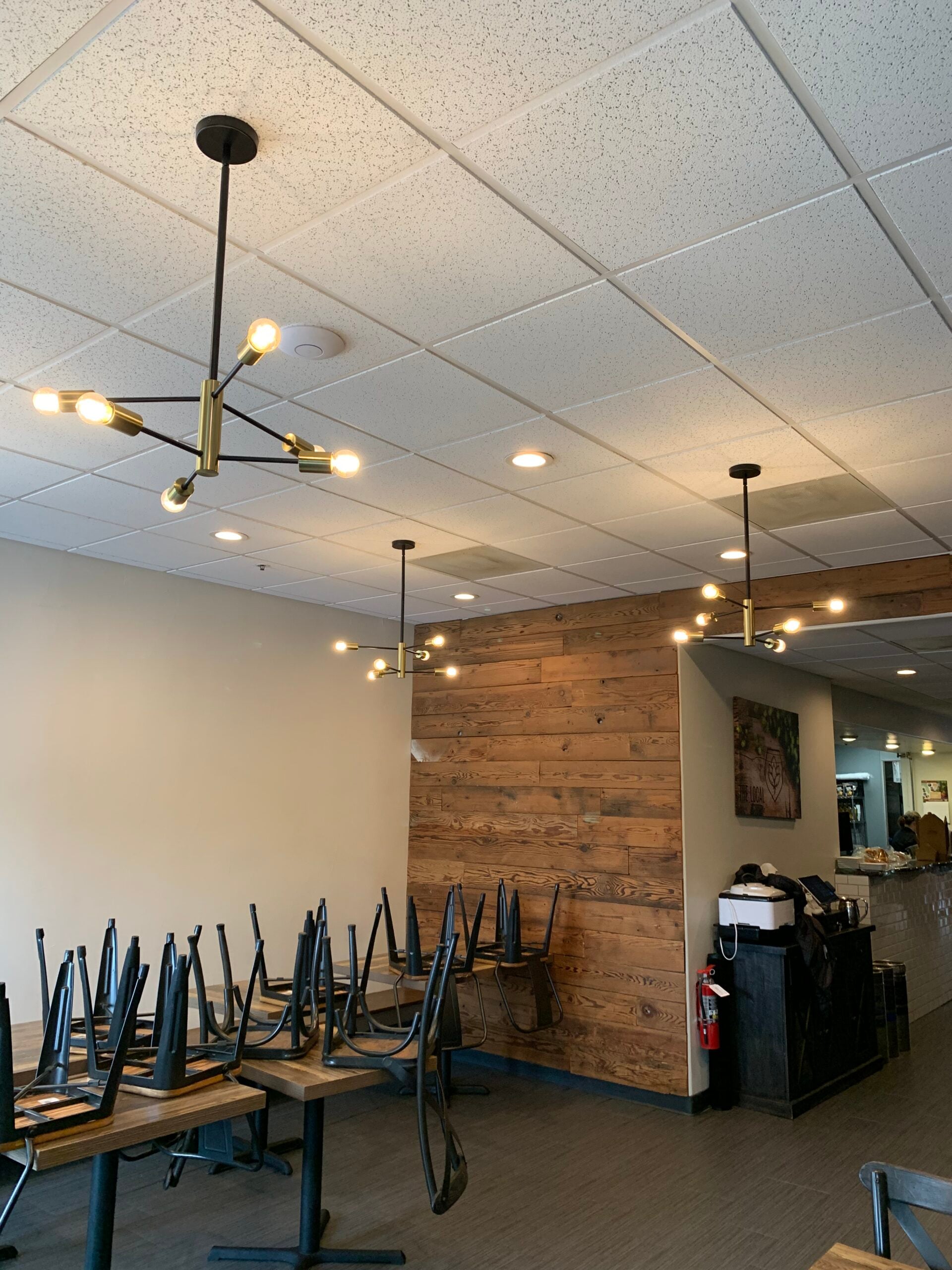 Modern brass and black sputnik chandeliers mounted to a drop ceiling in a restaurant dining area.