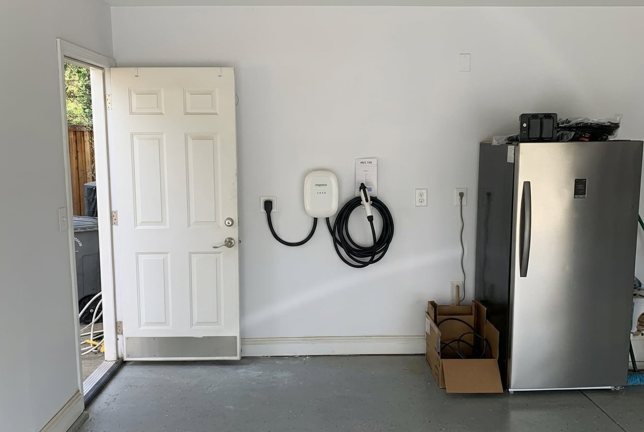 Wall-mounted Level 2 EV charging station with coiled charging cable installed inside a residential garage next to a doorway.